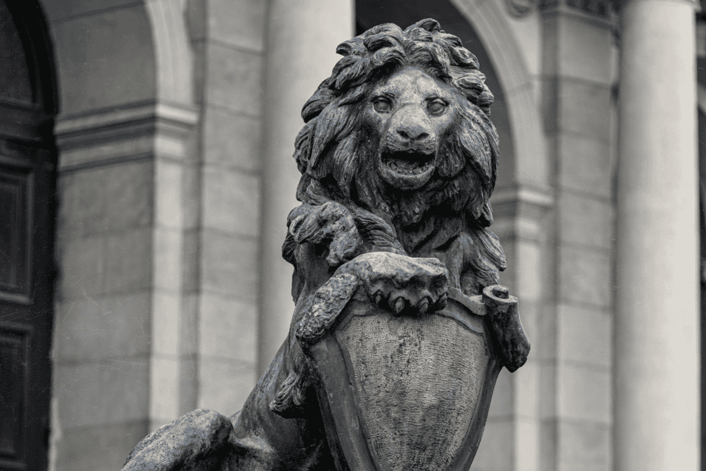 A black-and-white stone lion statue holding a heraldic shield outside a classical building