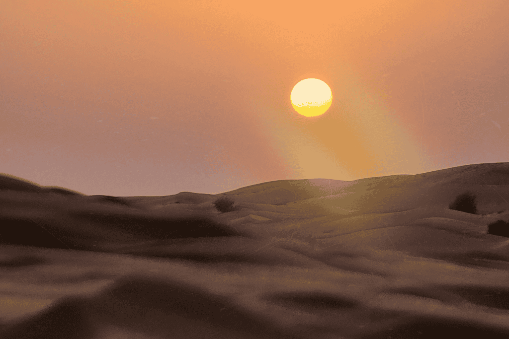 The sun glowing low over rolling sand dunes at dusk