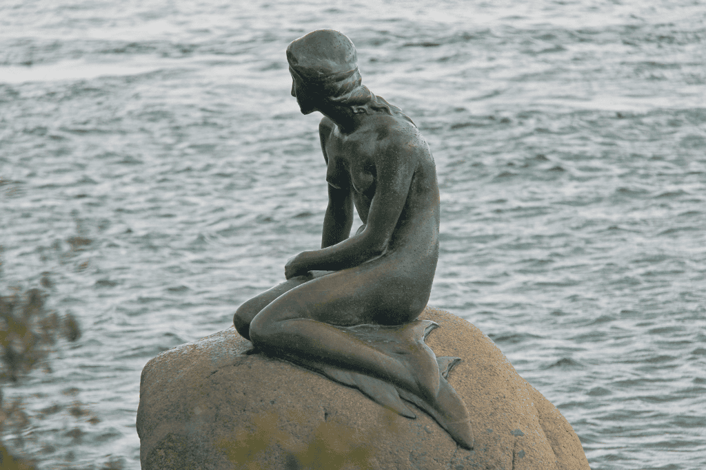 The bronze Little Mermaid statue seated on a rock beside grey water