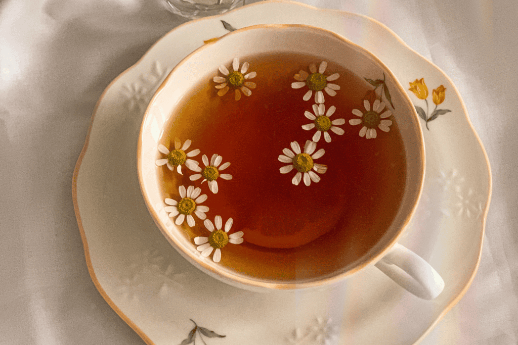 A floral teacup of amber tea with chamomile blossoms floating on top